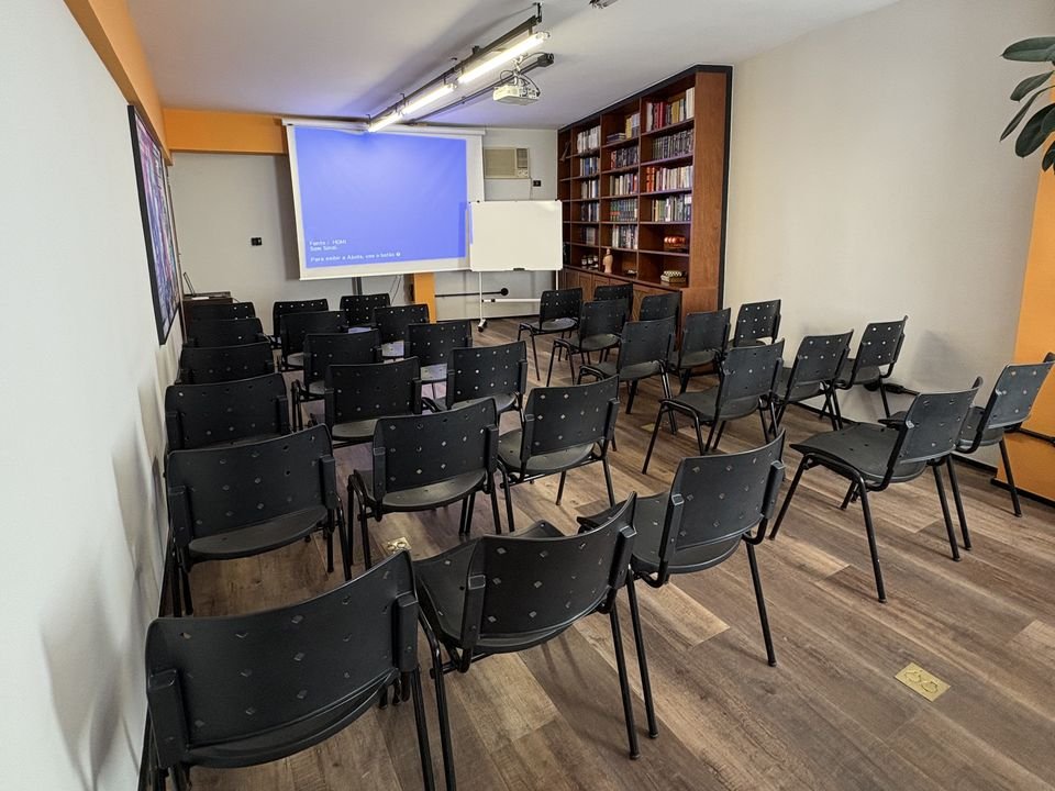 Auditório montado com fileiras de cadeiras e tela de projeção